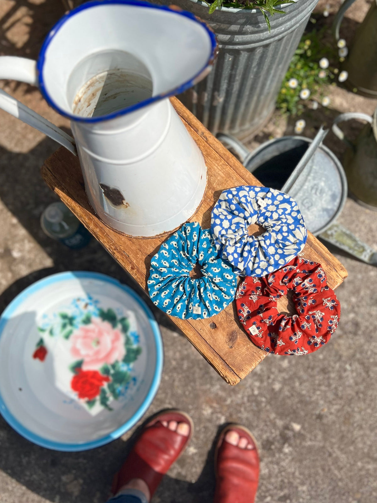 White pitcher with blue rim on a wooden block, surrounded by decorative items including a floral plate and patterned coasters.